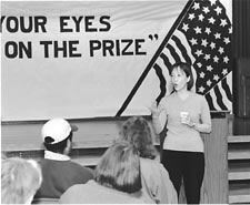 Wilma Chan speaking , a sign in the background states -Keep your eyes on the prize